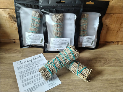Bundles of sage on a wooden surface with packaging and a cleansing guide.